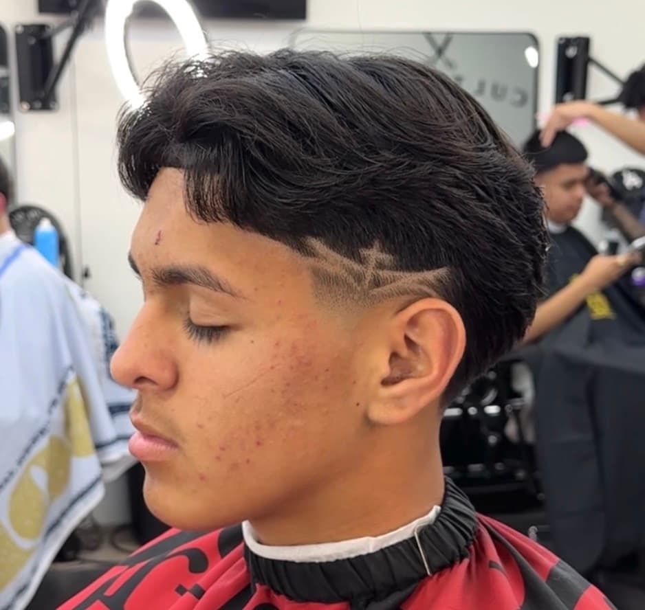 Young man with a textured wavy haircut and a shaved cross design on his temple.