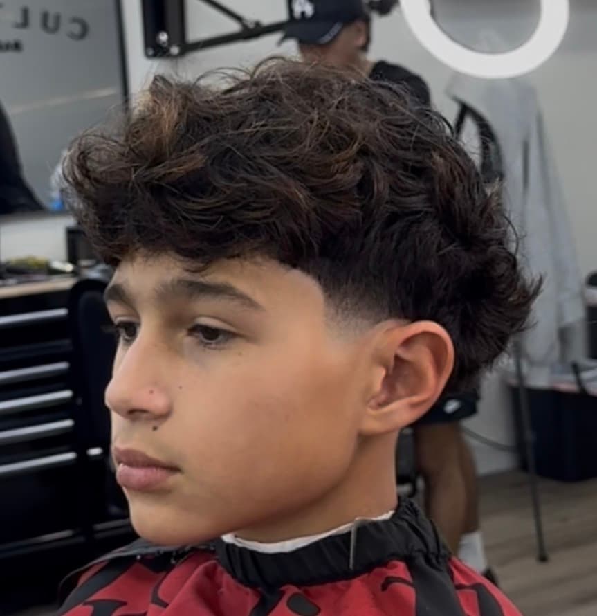 Young boy with a messy curly fringe haircut and a clean low taper fade.