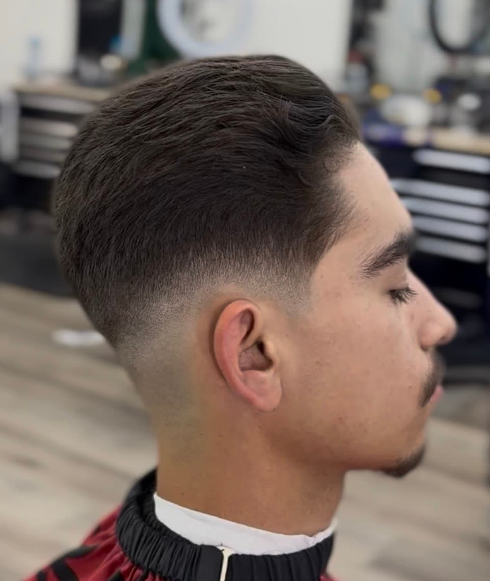 Side profile of a man with a sharp mid-skin fade and textured, wavy dark hair.