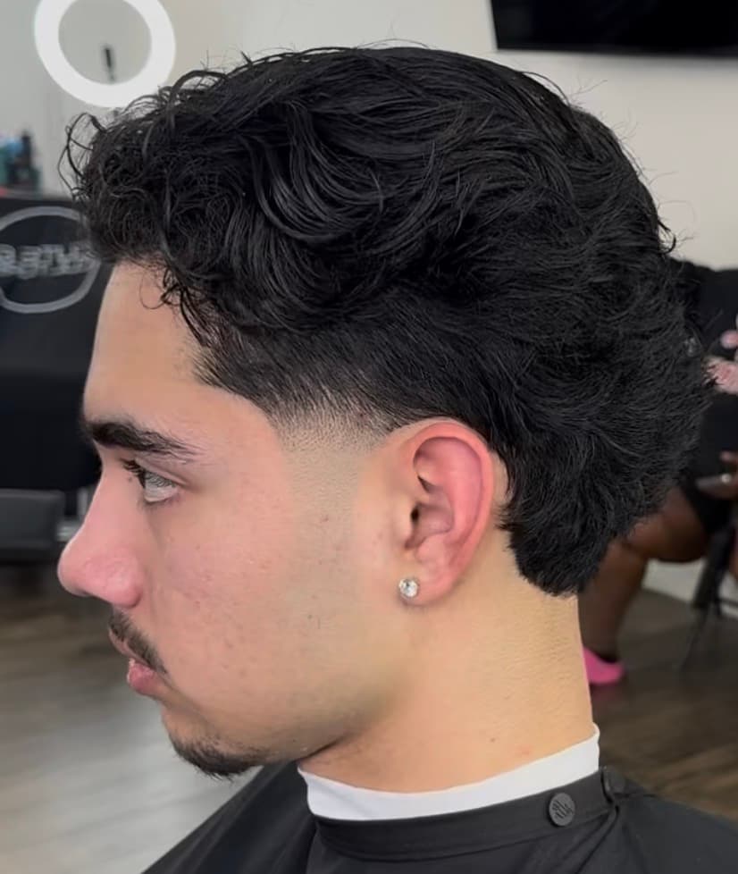 Side profile of a man with dark wavy hair and a fresh taper fade haircut.