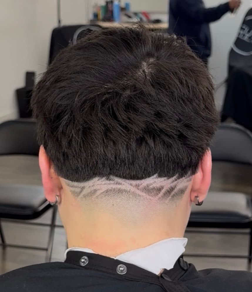 Textured dark hair with a sharp horizontal cut and geometric patterns shaved into the nape.
